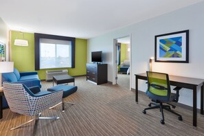 A hotel room with a large window, a blue sofa, a patterned armchair, a desk, and a television. - Holiday Inn Express & Suites Effingham by IHG (Effingham)