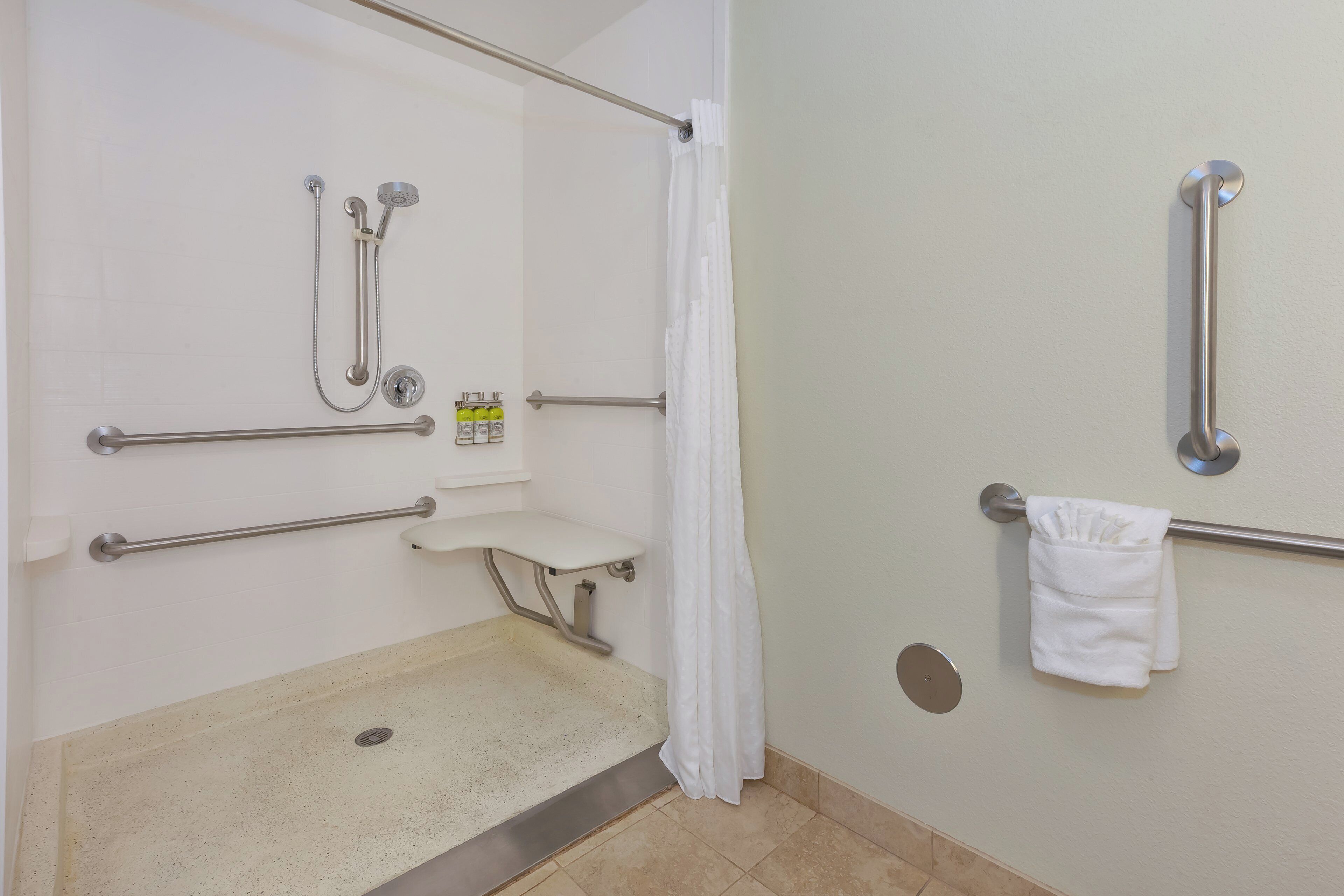 Un bagno accessibile ai disabili con doccia, maniglie di sostegno, seduta e porta asciugamani.