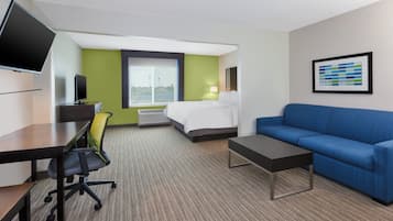 Habitació d'hotel amb un llit, un escriptori amb un ordinador, un sofà blau i una finestra gran.
