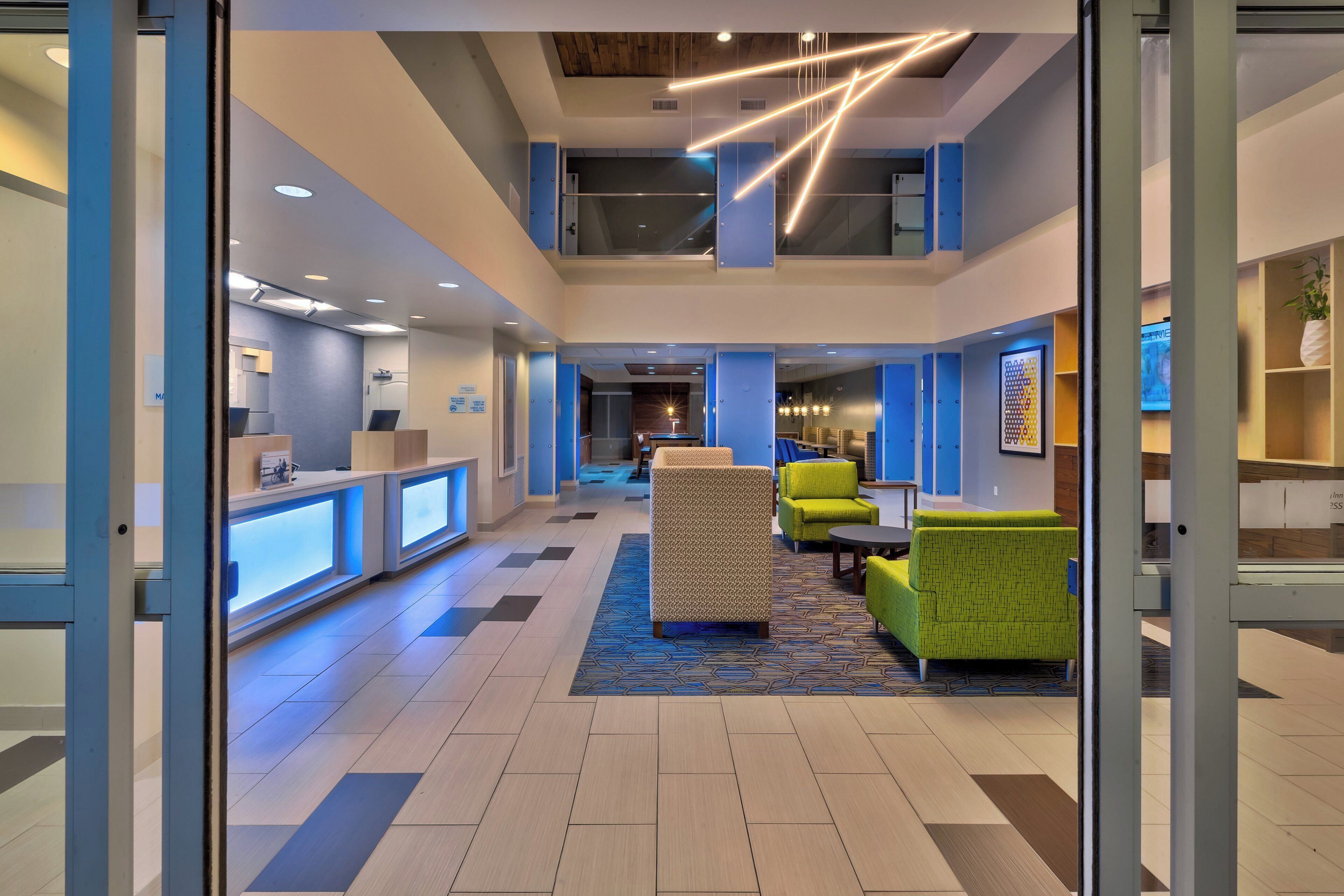 A modern lobby with a reception desk, seating area, and a staircase leading to an upper level.
