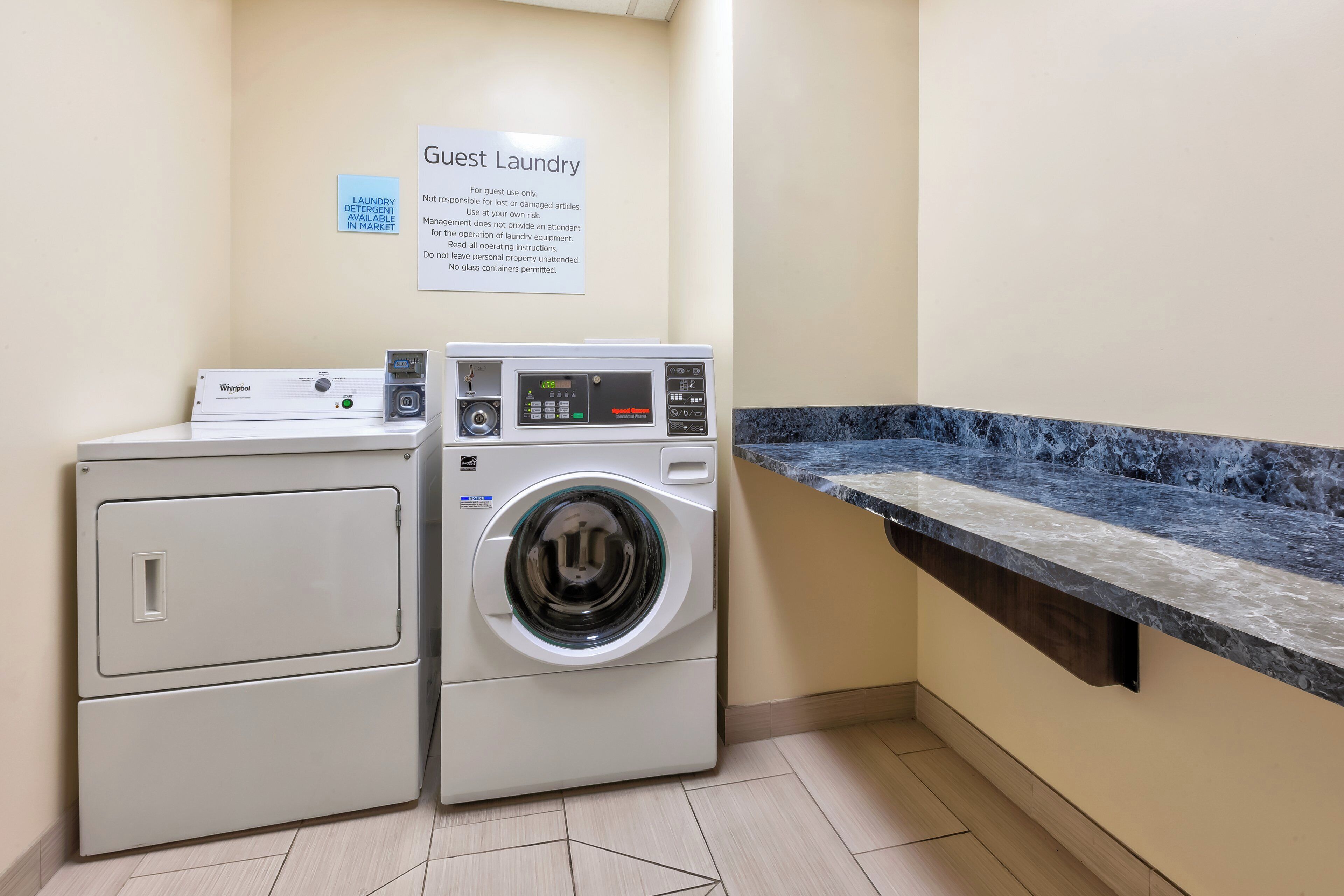 A guest laundry area with a Whirlpool washer and dryer, a sign indicating laundry detergent is in market, and a marble countertop.