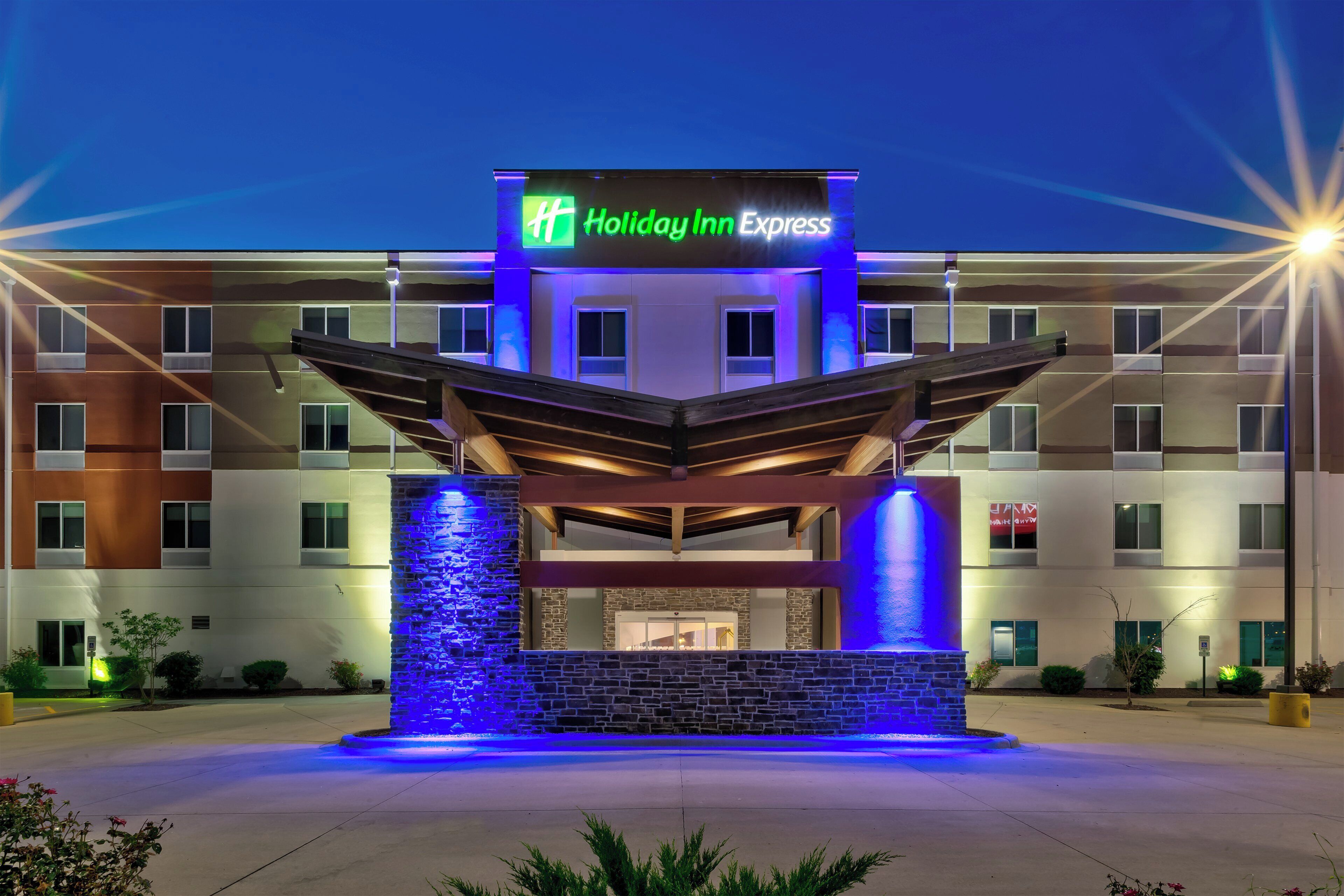 Ein Holiday Inn Express Hotel mit einem modernen Eingang, der eine Steinfassade und blaue Beleuchtung aufweist.