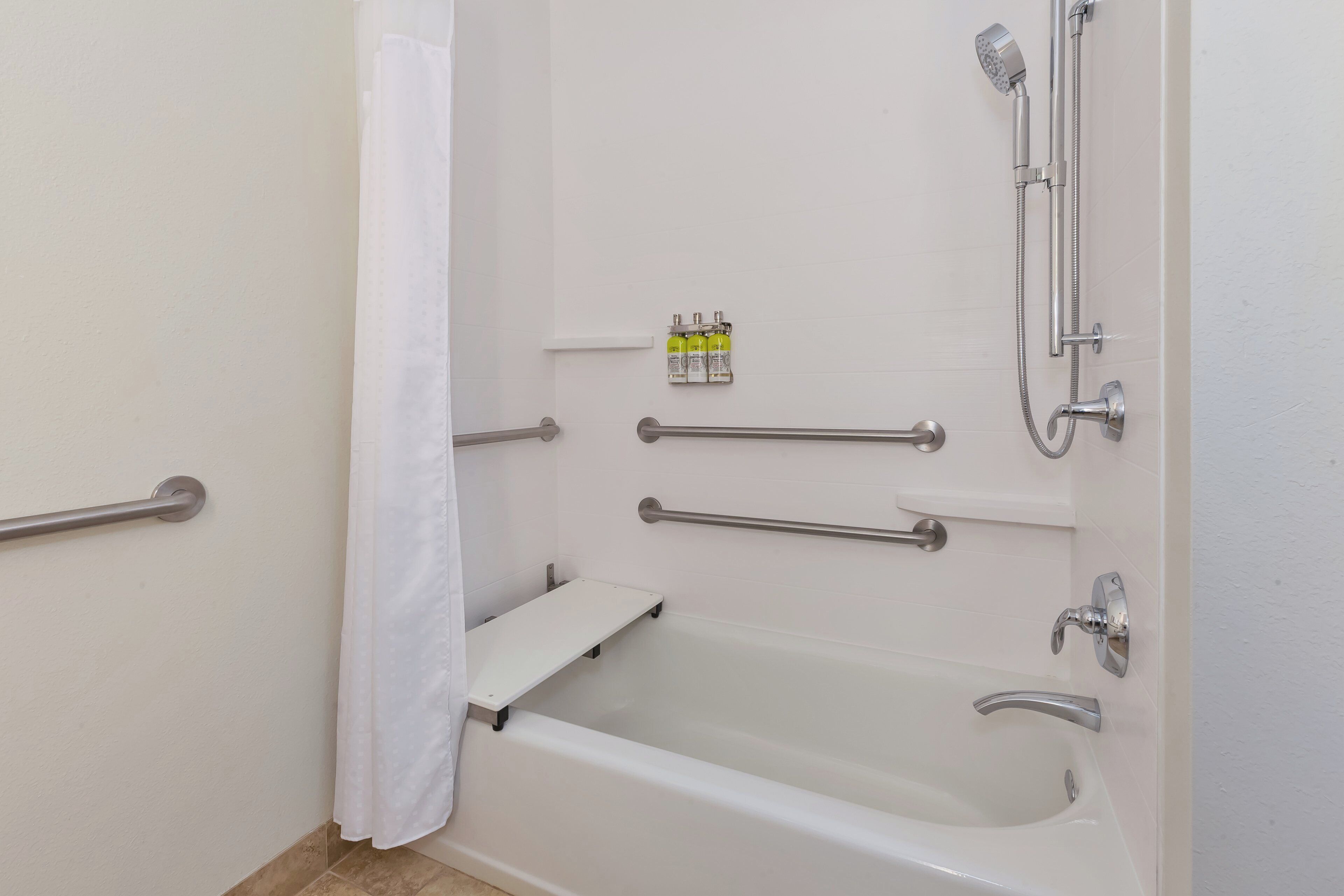 A bathroom with a bathtub, grab bars, a showerhead, and a shelf with toiletries.