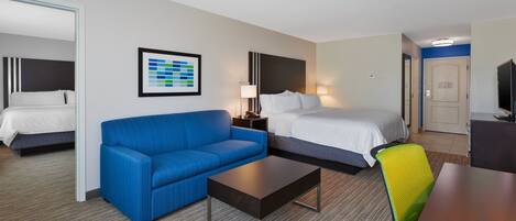 Una habitación de hotel con una cama, un sofá azul, una mesa de centro y un televisor.
