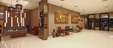 A spacious lobby with a modern design, featuring a reception desk, seating area with sofas and chairs, and decorative wall art.