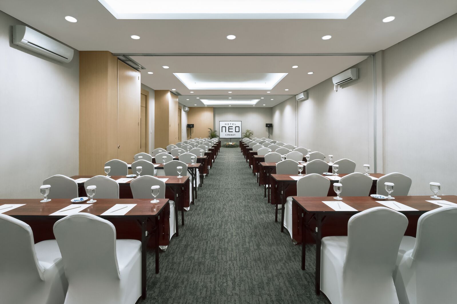 Una sala conferenze con file di tavoli e sedie, condizionatori d'aria e un cartello con il nome dell'hotel.