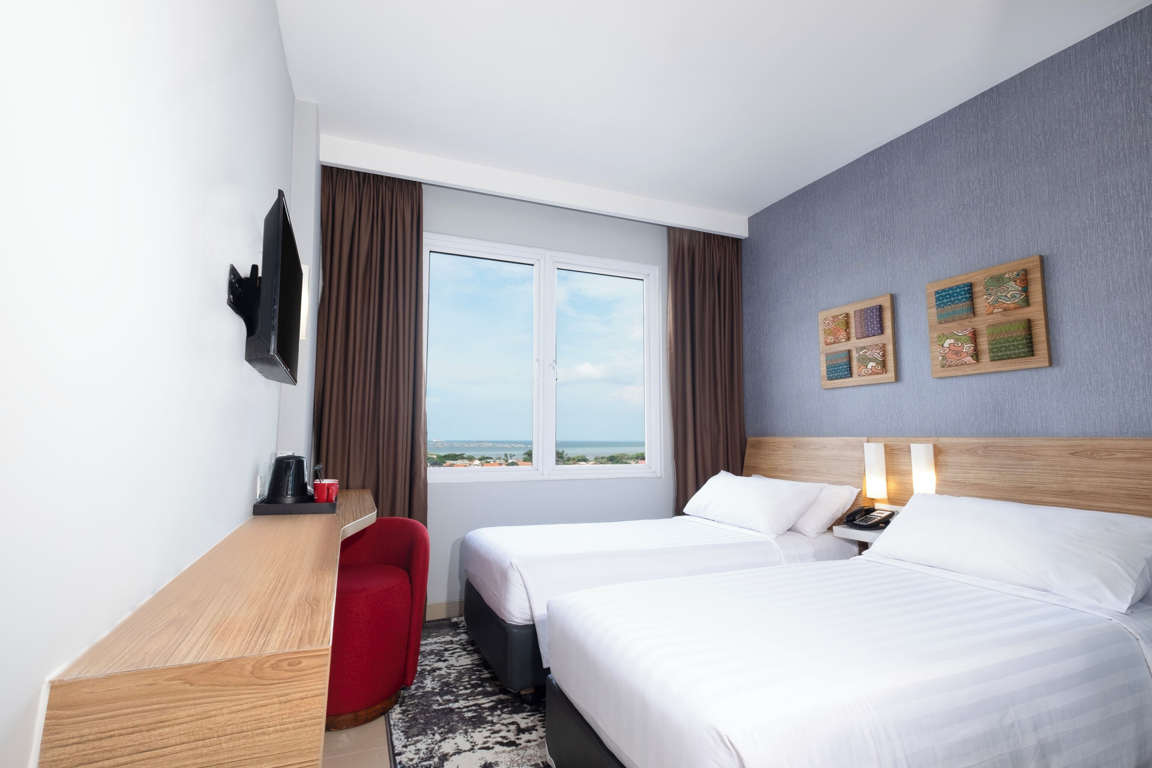 Habitación de hotel con dos camas, un escritorio, una silla, un ventanal y decoración en las paredes.