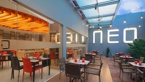 Un restaurante moderno con divisiones de vidrio, sillas rojas y negras, y un gran letrero iluminado.