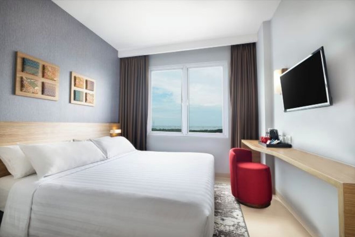 Habitación de hotel con cama, televisor montado en la pared, ventana con vistas y un pequeño escritorio con silla.
