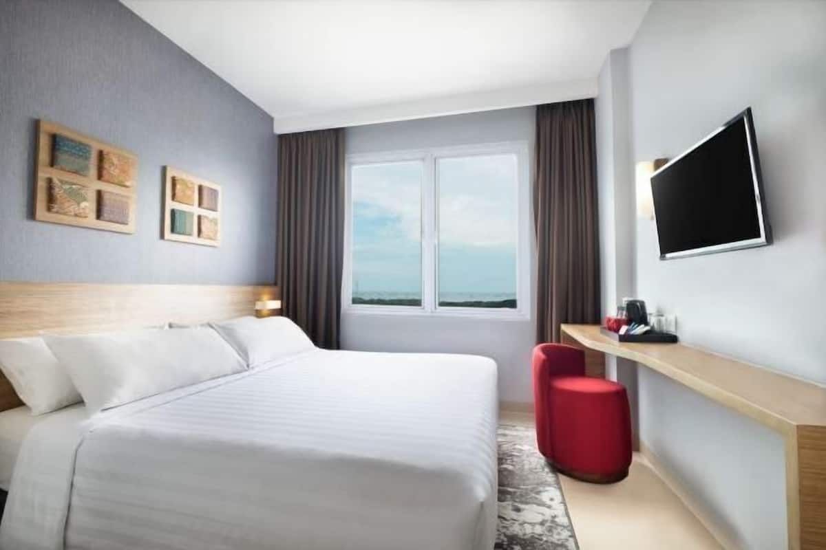 Une chambre d’hôtel avec un lit, un téléviseur fixé au mur, une fenêtre donnant sur un paysage agréable et un petit bureau avec une chaise.