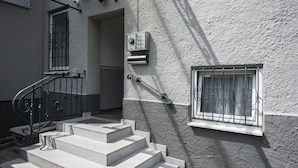 A set of stone steps leading to a door, a window with metal bars, and a security intercom system on a textured wall.
