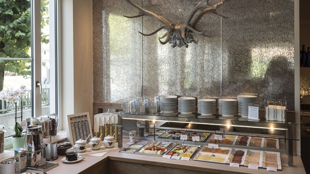 A breakfast buffet with various food items, a decorative antler piece, and a view of the outdoors.