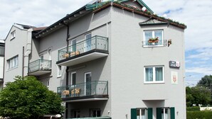 A multi-story building with balconies, a visible sign indicating a business, and a tree in front.
