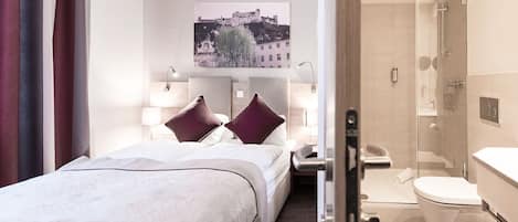 Une chambre d’hôtel avec un lit, des lampes de chevet, un tableau représentant un château, une douche et des toilettes.