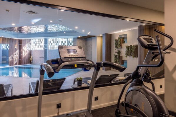 A modern gym with a stationary bike, a treadmill, and a pool visible through the glass wall.