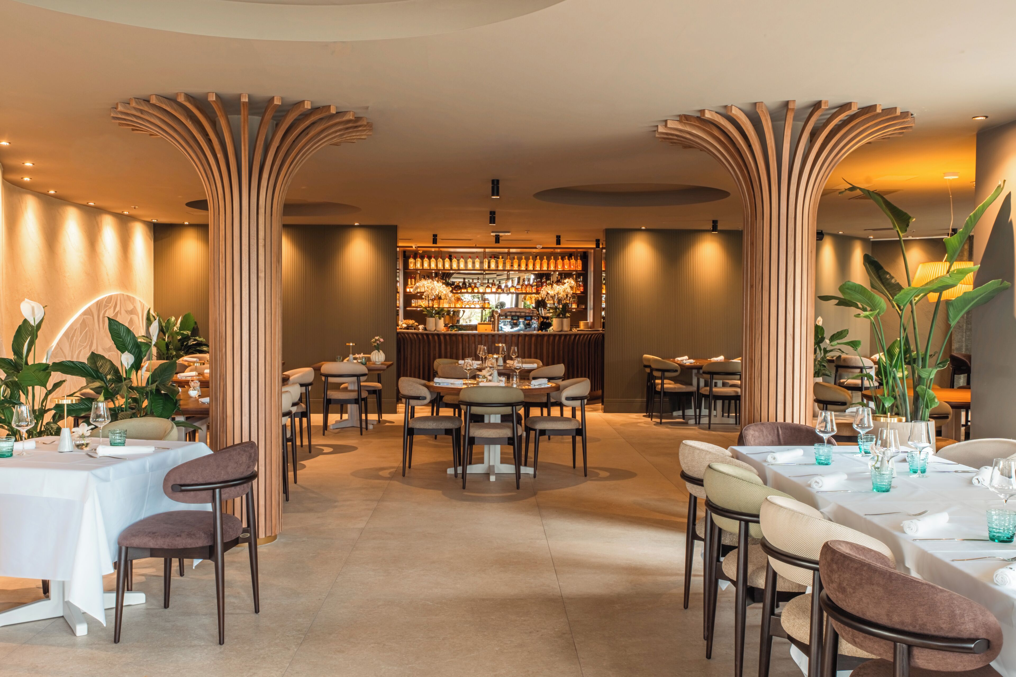 A restaurant with a bar area, tables, chairs, and decorative plants.