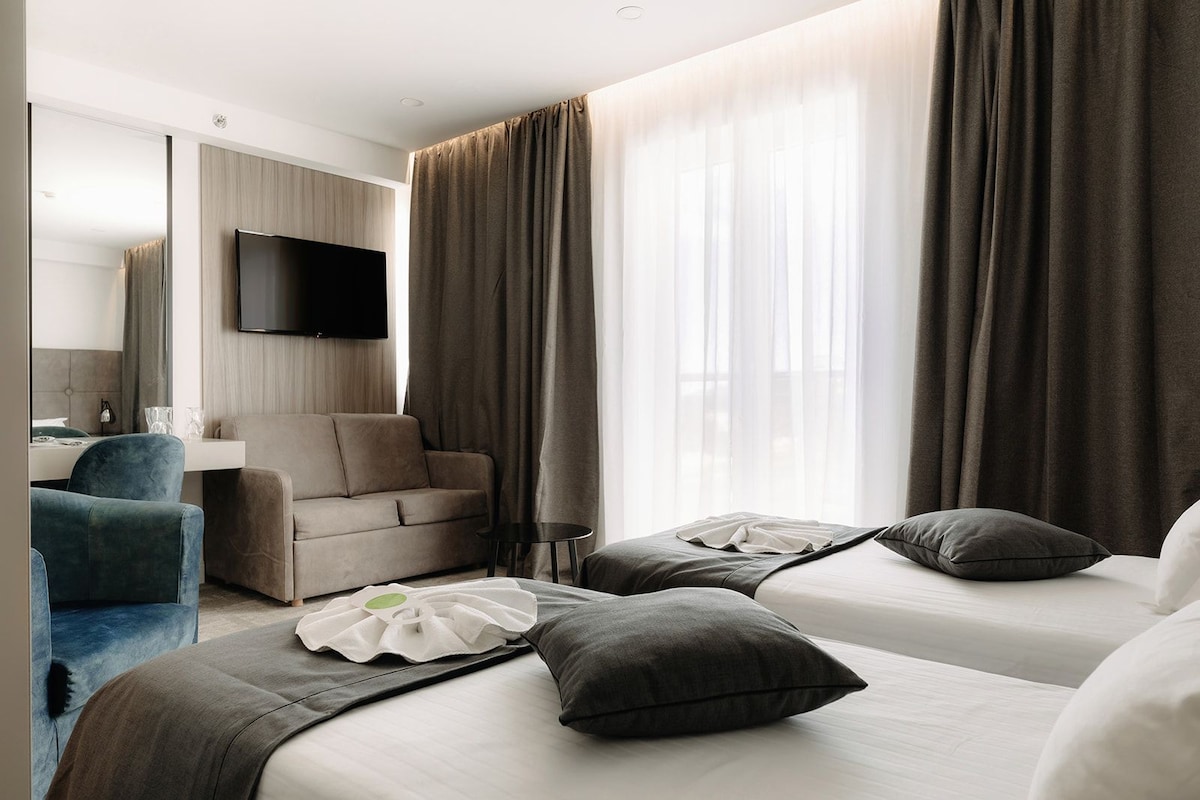 A hotel room with two beds, a sofa, a TV, and a desk.