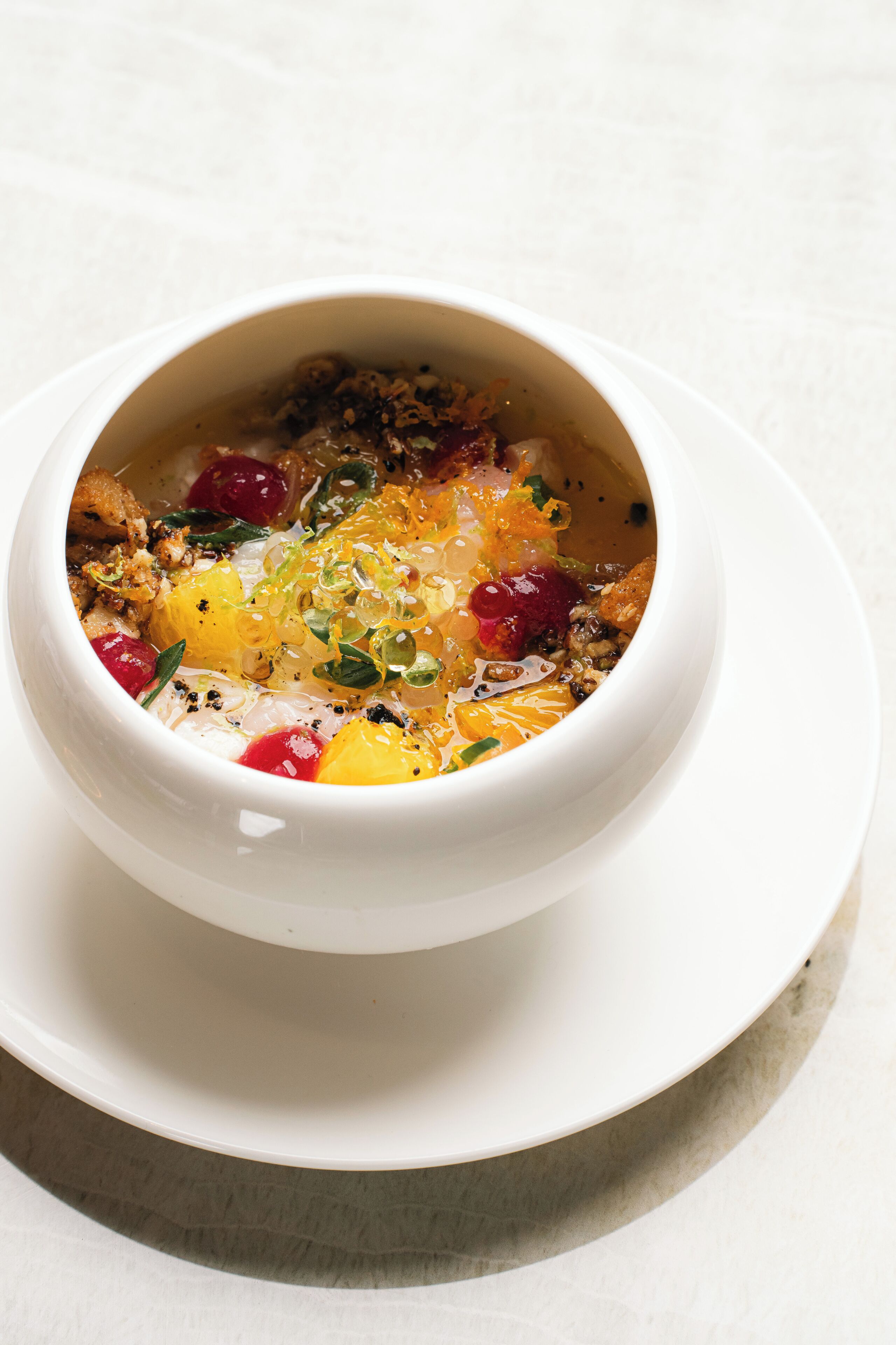 A white bowl of soup with various ingredients on a white plate.
