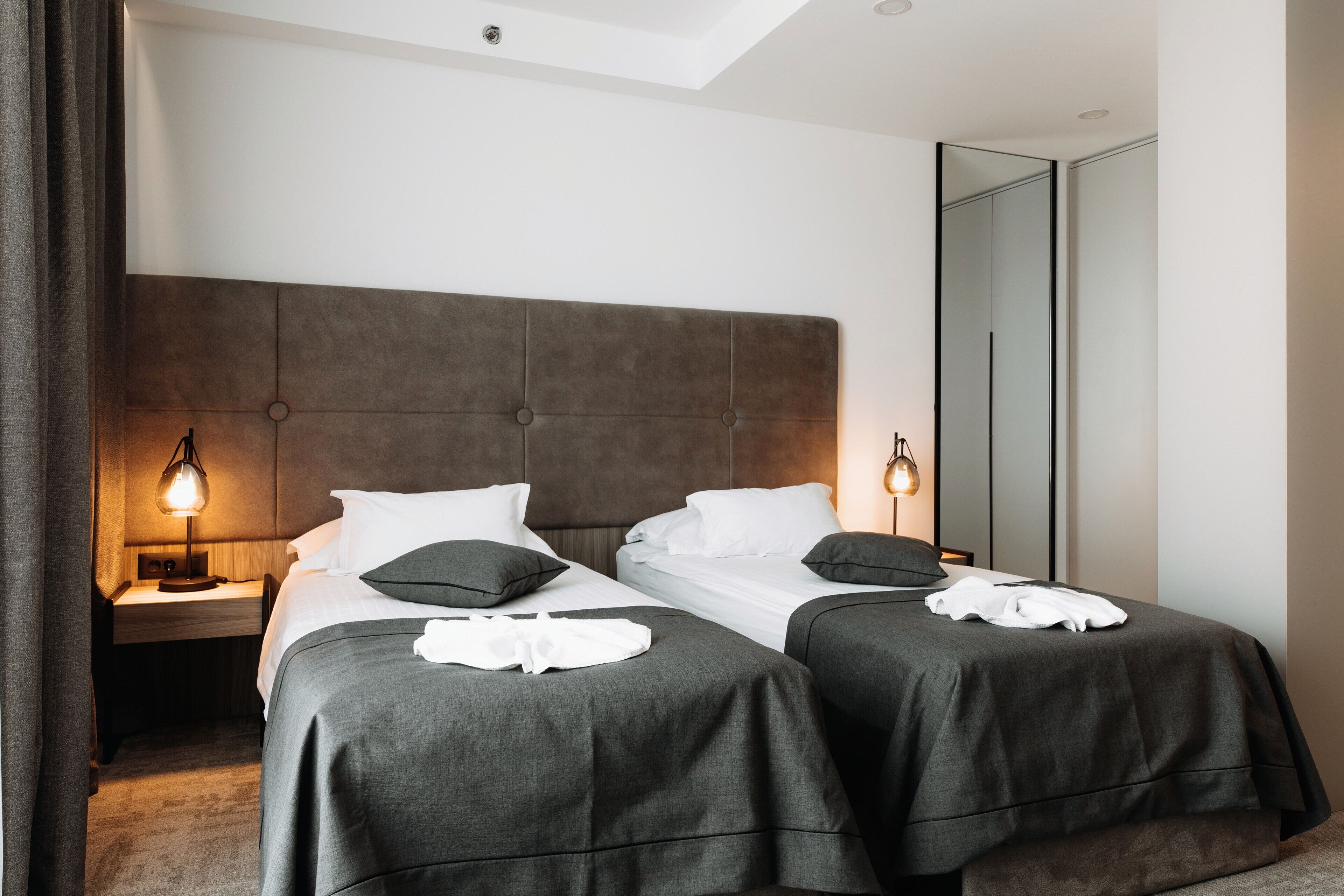 Una habitación de hotel con dos camas, un espejo grande y una mesita de noche con lámpara.
