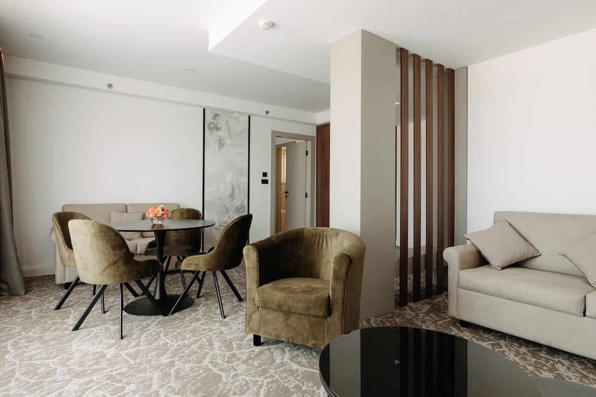 Ein modernes Wohnzimmer mit einem runden Esstisch, zwei Sesseln, einem Sofa und einem schwarzen Couchtisch.