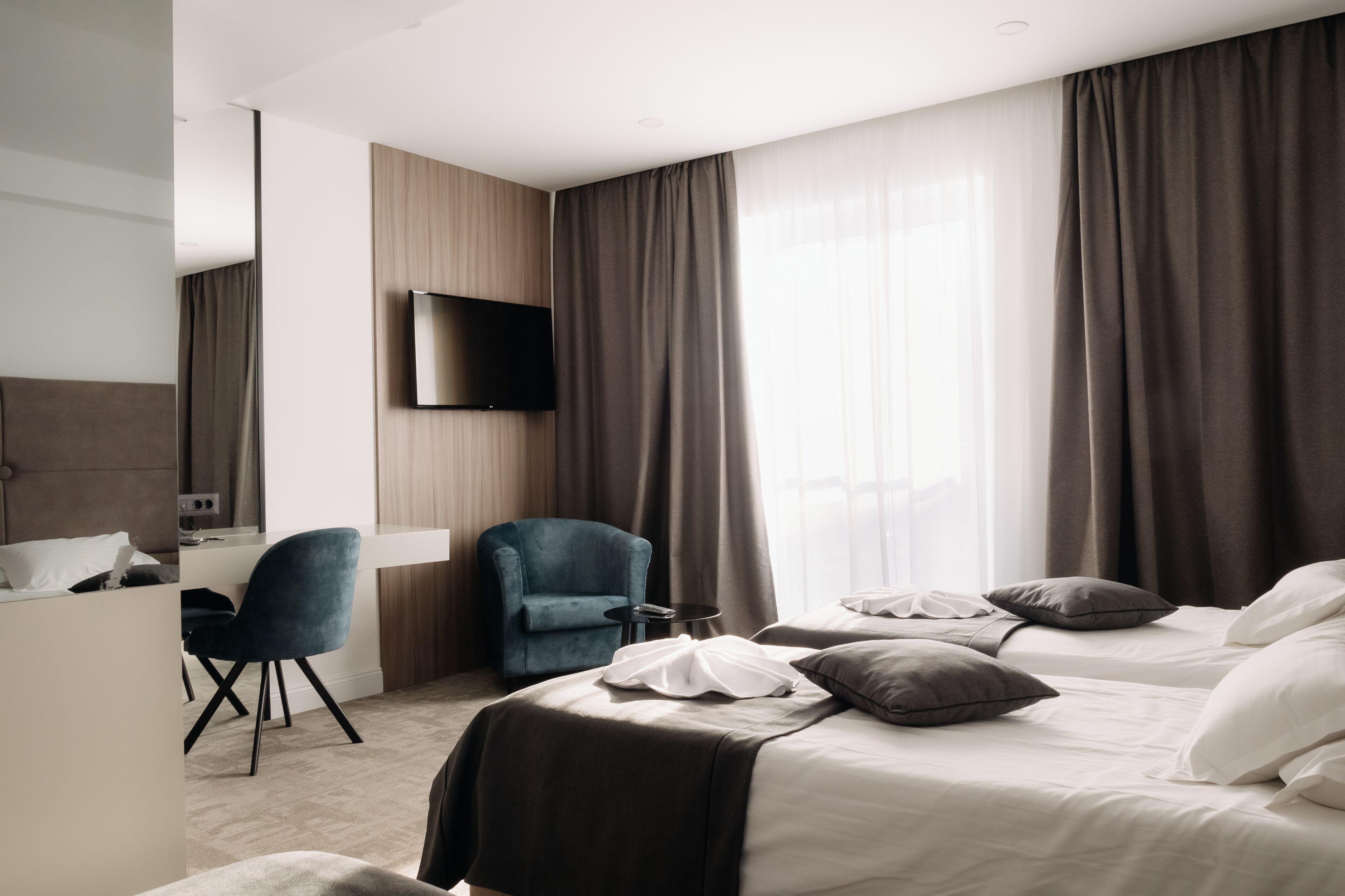 A hotel room with a bed, a desk, a chair, and a TV mounted on the wall.