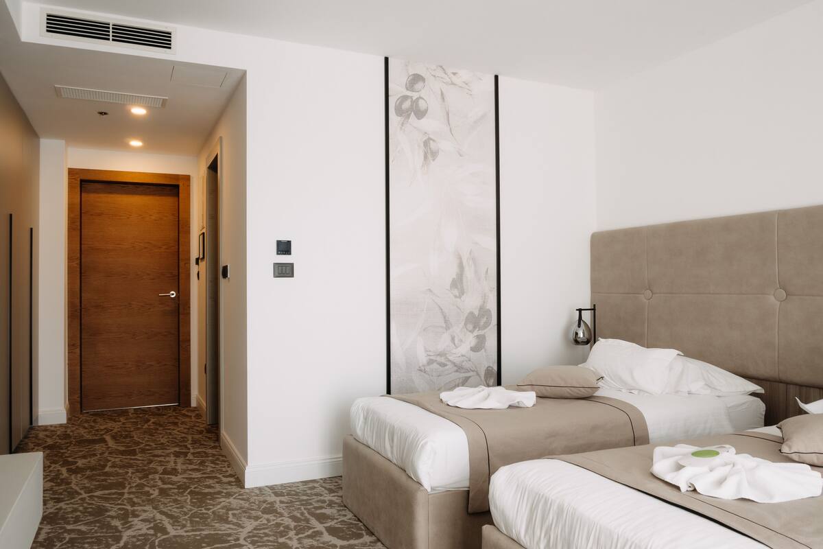 Ein Hotelzimmer mit einem großen Bett, einem kleineren Bett, einer Holztür und einer Wand mit floralem Dekor.