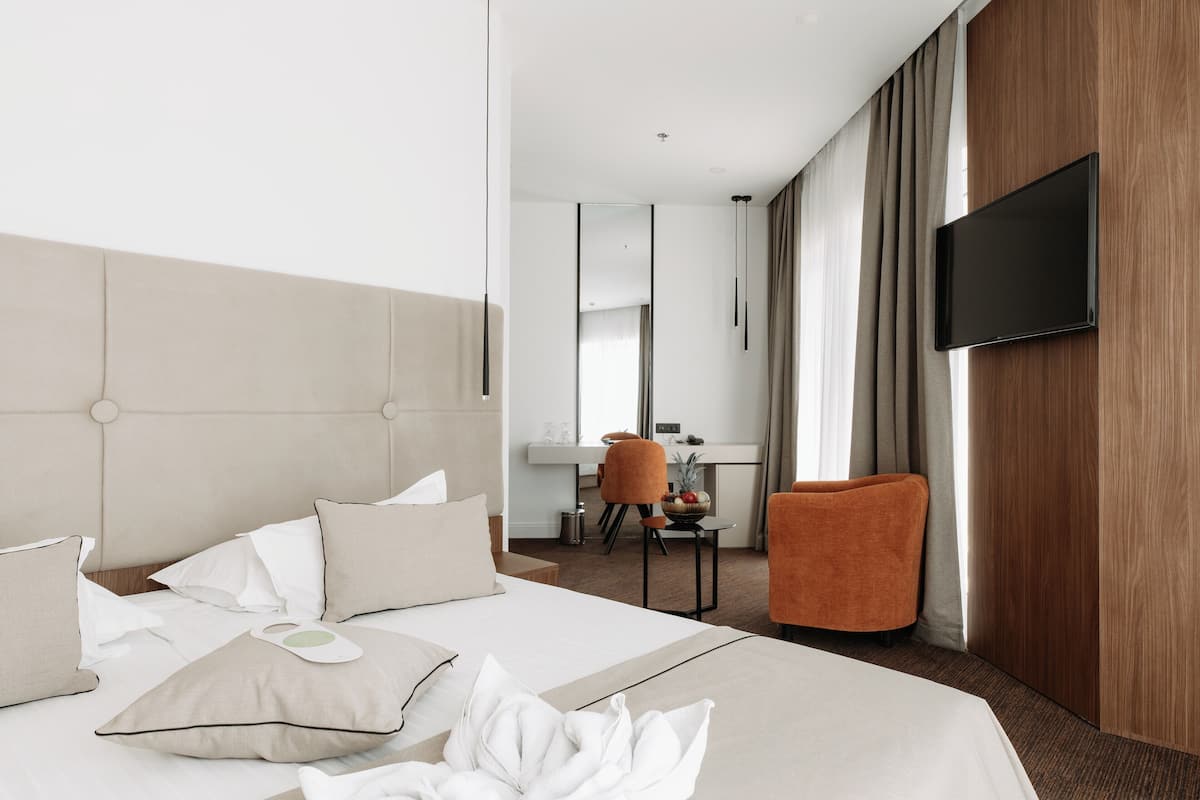 Ein Hotelzimmer mit einem großen Bett, einem Schreibtisch und einem an der Wand befestigten Fernseher.