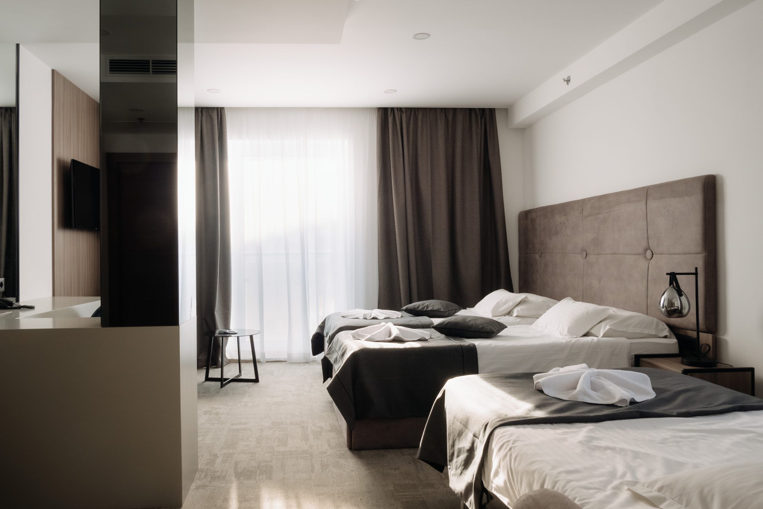 A hotel room with a bed, bedside table, lamp, and a TV mounted on the wall.