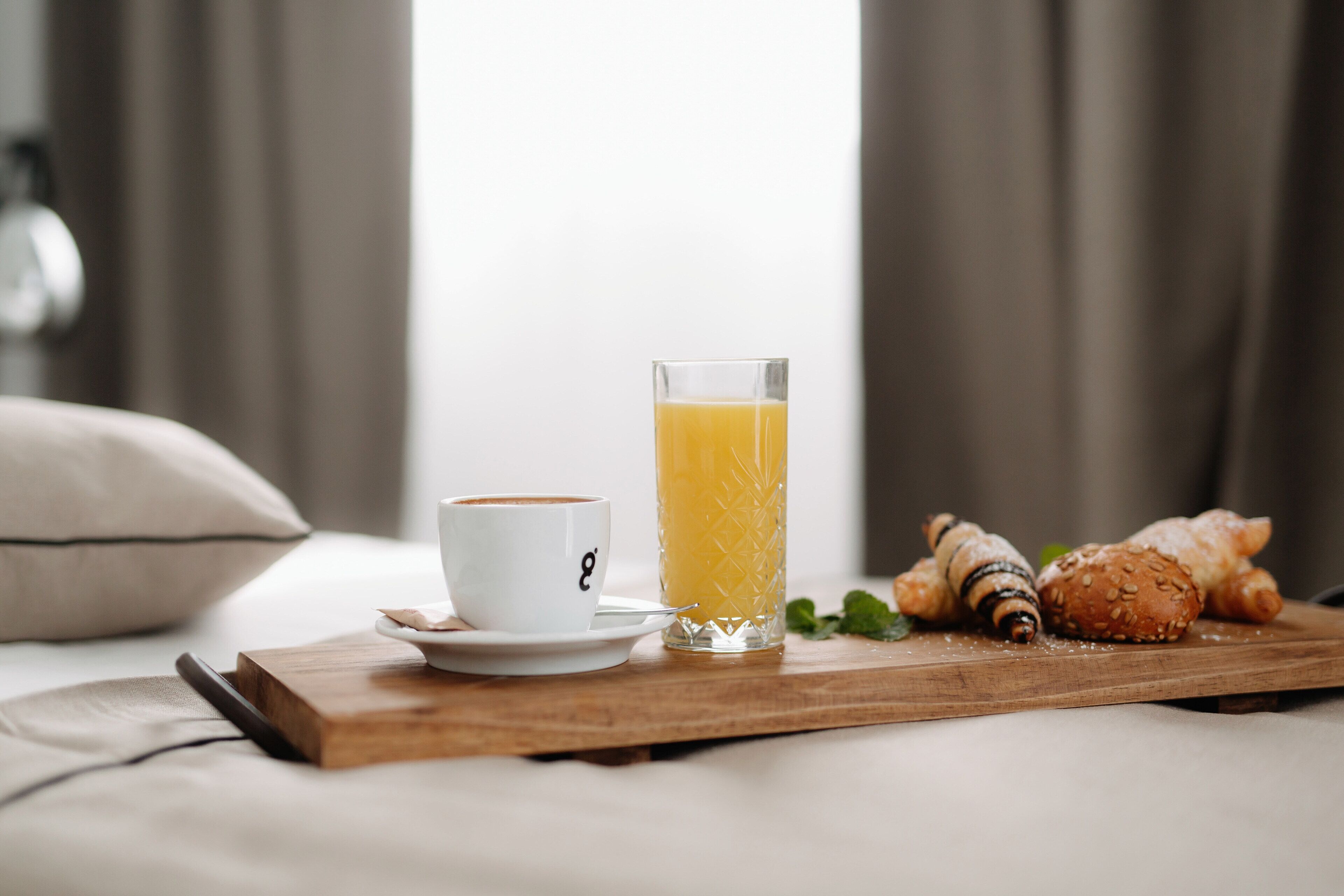 A breakfast tray with a glass of orange juice, a cup of coffee, croissants, and a pastry on a wooden board.