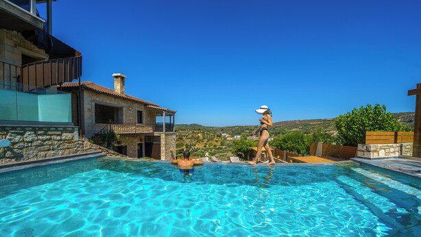 A swimming pool with clear blue water, surrounded by stone buildings and a view of the countryside. - Asion Lithos (Heraklion)