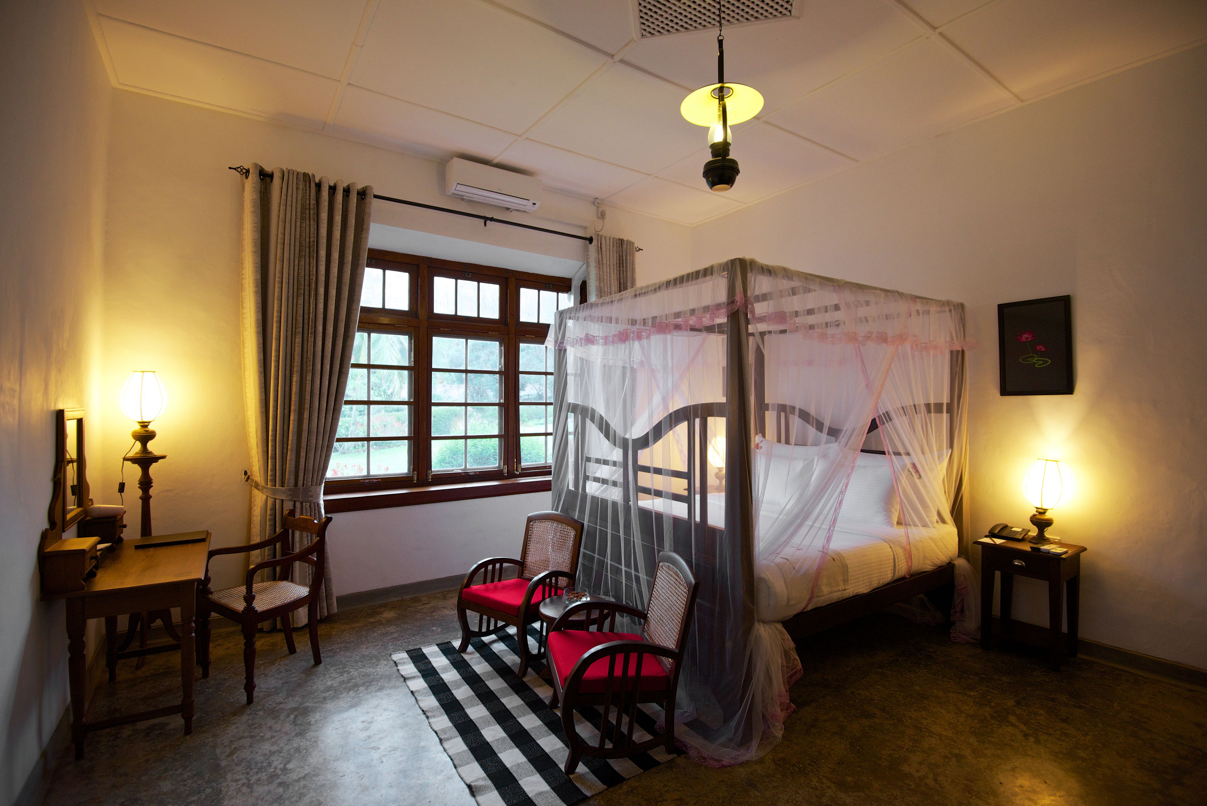 Ein Schlafzimmer mit Himmelbett, Schreibtisch mit Stuhl, Nachttisch mit Lampe und einem Fenster mit Vorhängen.