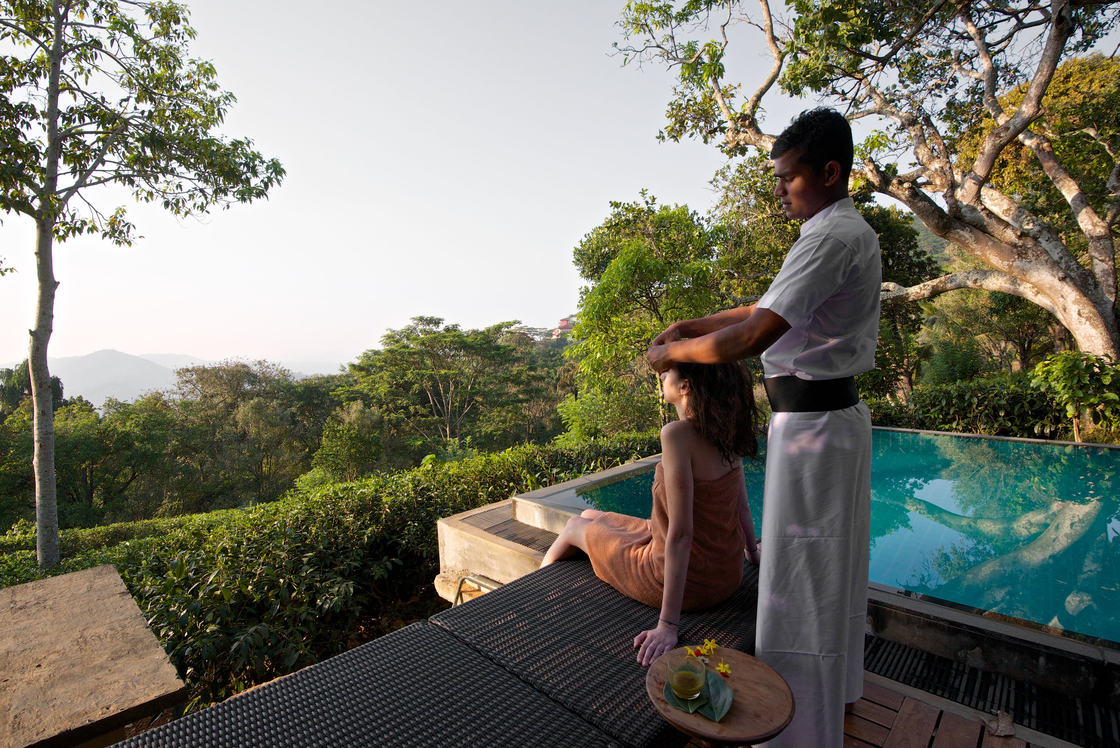 A person performing a head massage on another individual by a poolside.