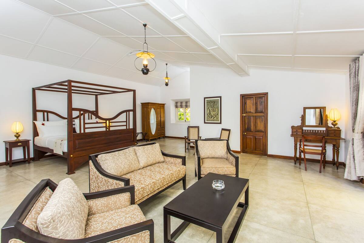 Una habitación amplia con una cama con dosel, un sofá, una mesa de centro y un escritorio con una silla.