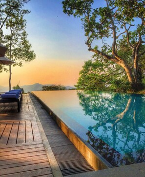 A serene infinity pool with wooden deck seating, surrounded by lush greenery and trees. - Mountbatten Bungalow (Kandy)