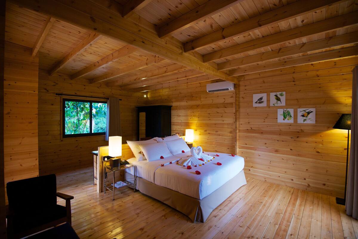Un dormitorio de cabaña de madera con una cama, lámparas de noche, una ventana y obras de arte colgadas en la pared.