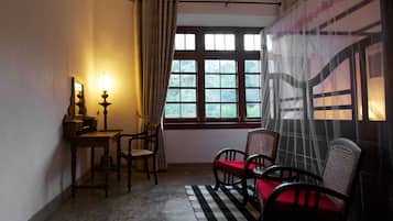 A room with a wooden desk, two chairs, a lamp, a window with a view of greenery, and a checkered rug.