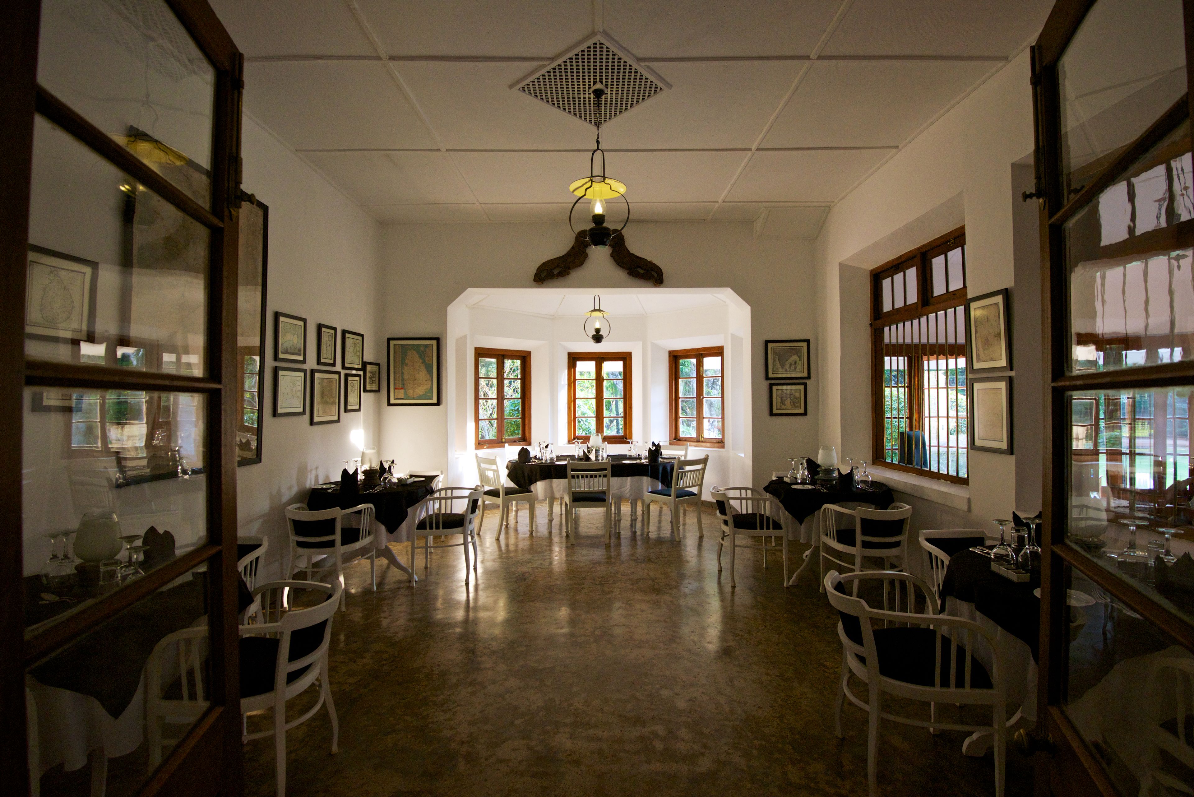 A dining area with a high ceiling, chandeliers, and framed artwork on the walls.
