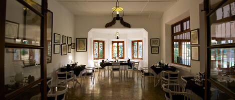 A dining area with a high ceiling, chandeliers, and framed artwork on the walls.