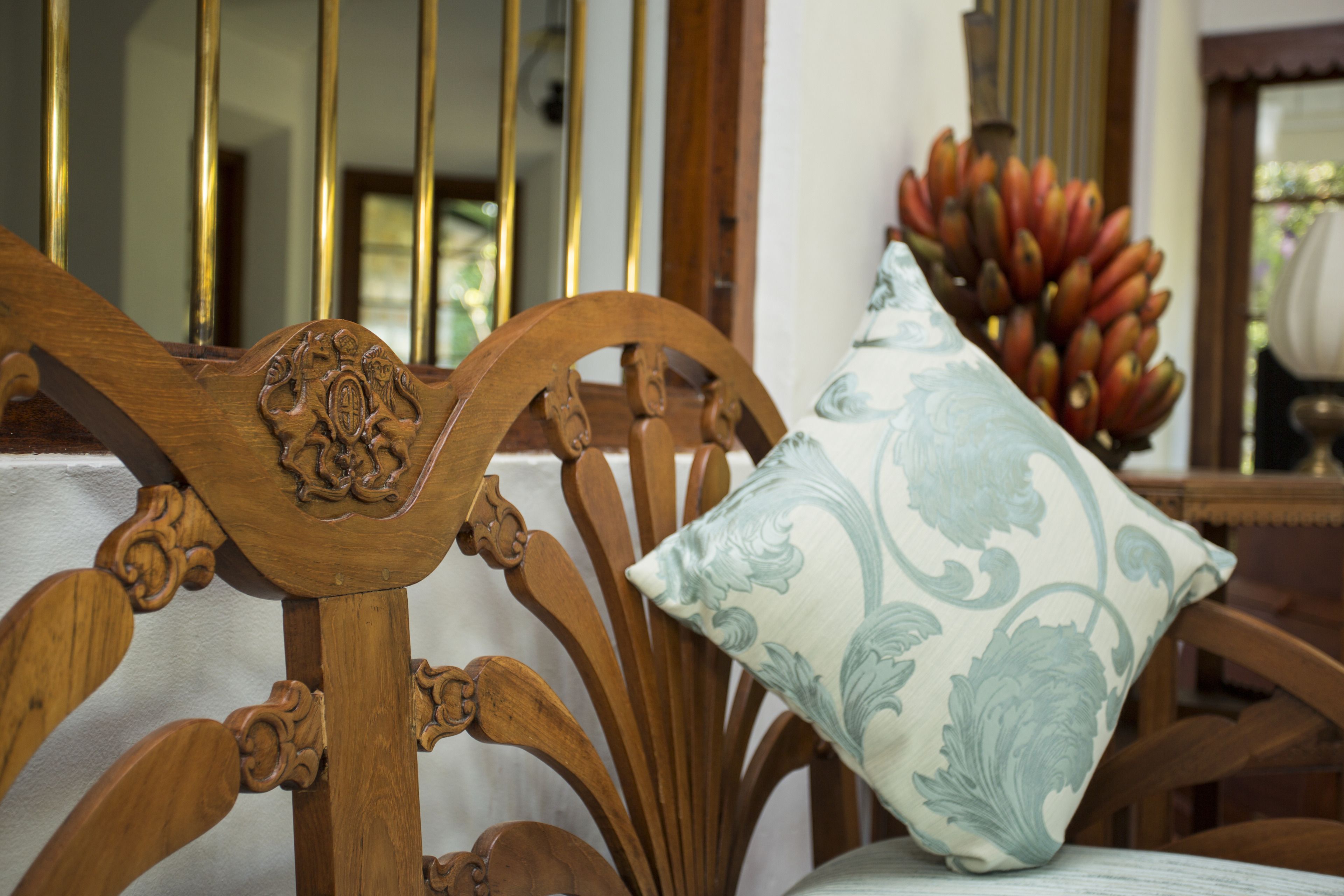A wooden chair with intricate carvings and a cushion with a floral pattern.