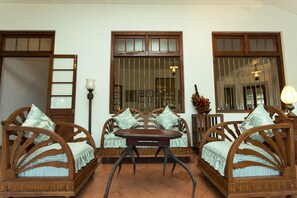 A traditional wooden sofa with a matching table in the center, flanked by two chairs, all set against a white wall with large windows.