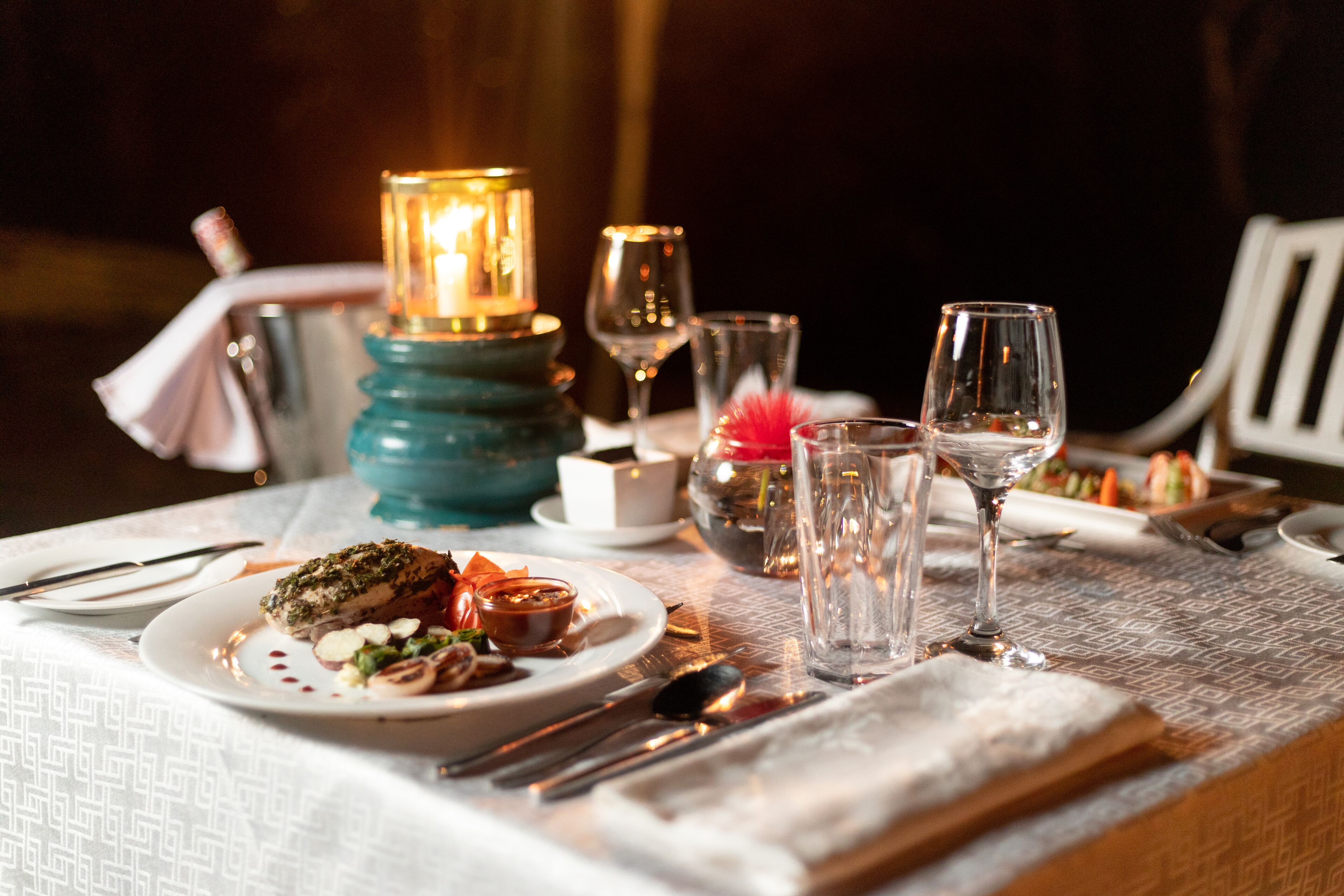 A table set for a meal with plates of food, cutlery, glasses, and a lit candle.
