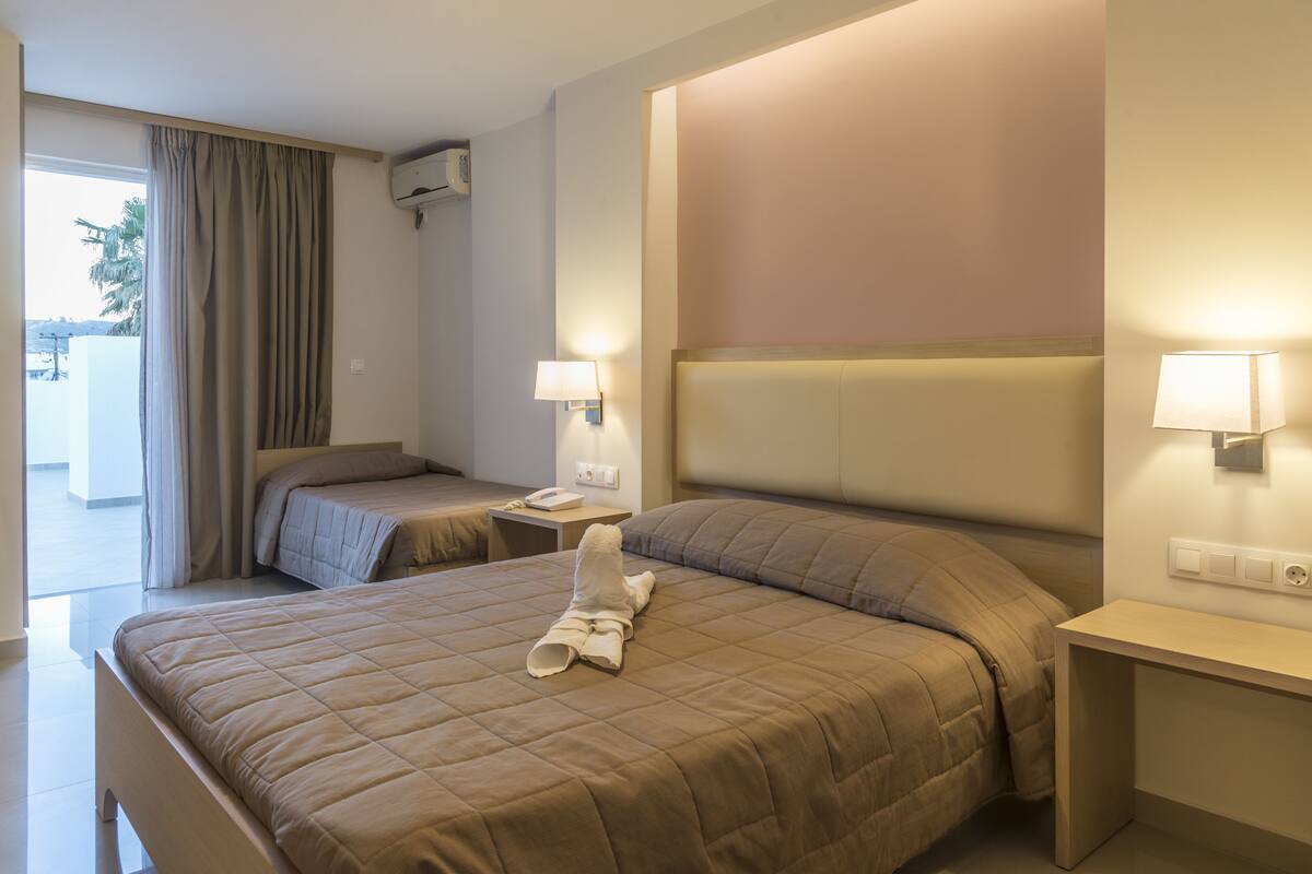 A hotel room with a large bed, a smaller bed, a desk, and a lamp.
