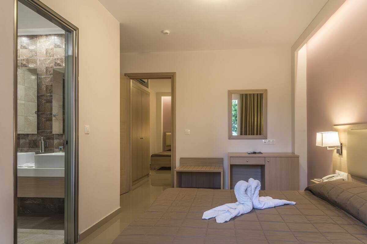 A hotel room with a large bed, a bedside table, a mirror, and a bathroom visible through an open door.