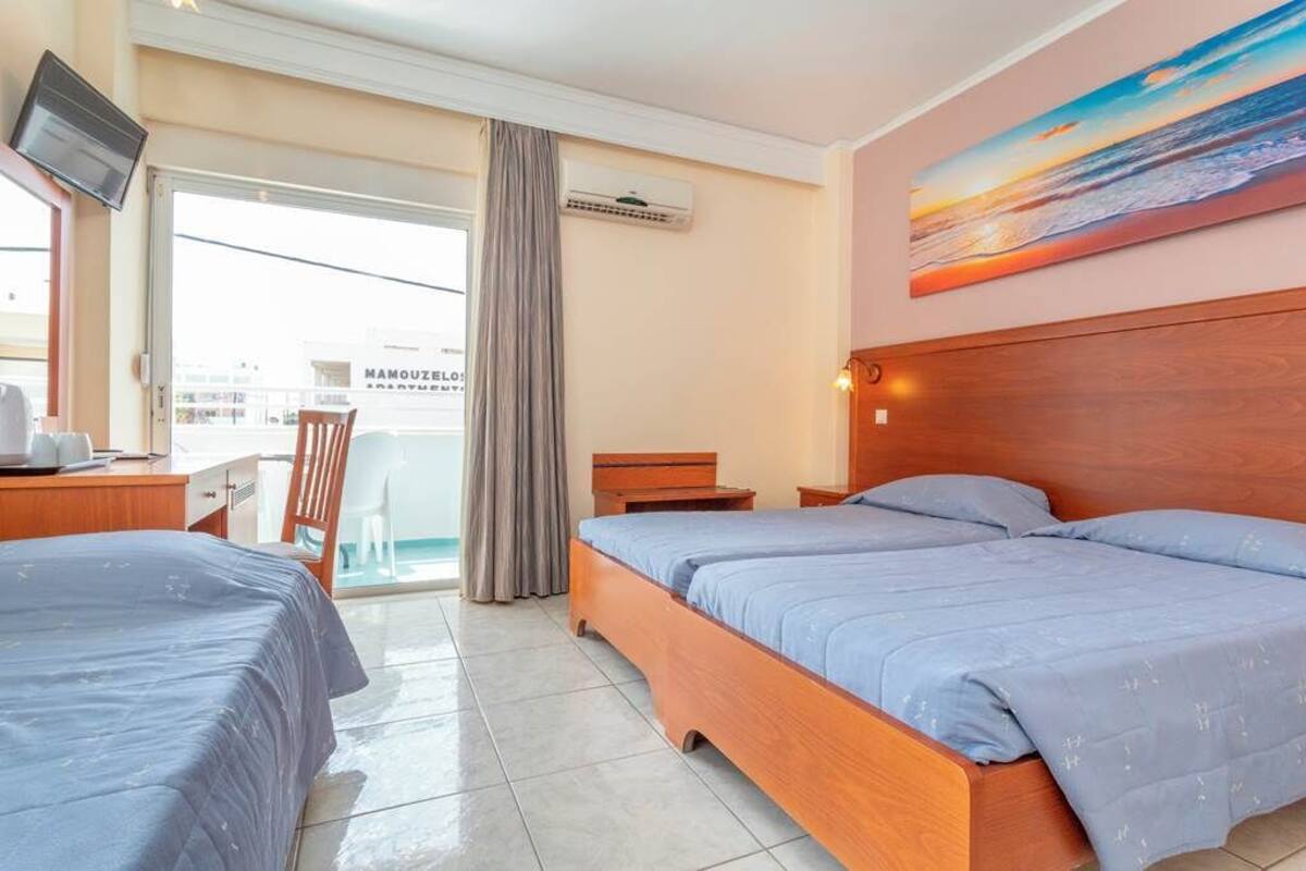 A hotel room with two beds, a desk, a chair, and a TV.