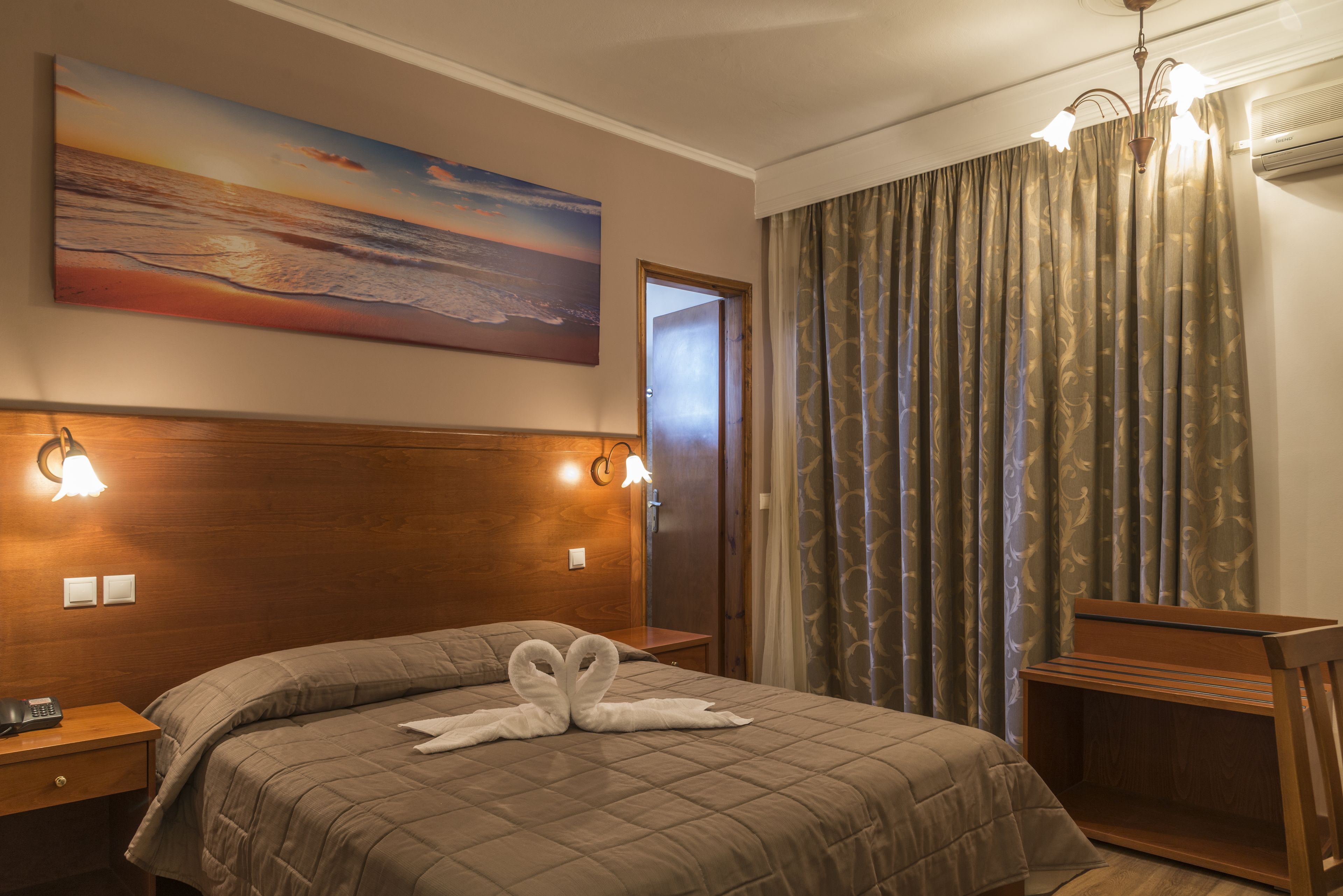Una habitación de hotel con una cama, un cuadro, una mesita de noche, una lámpara y una cortina.