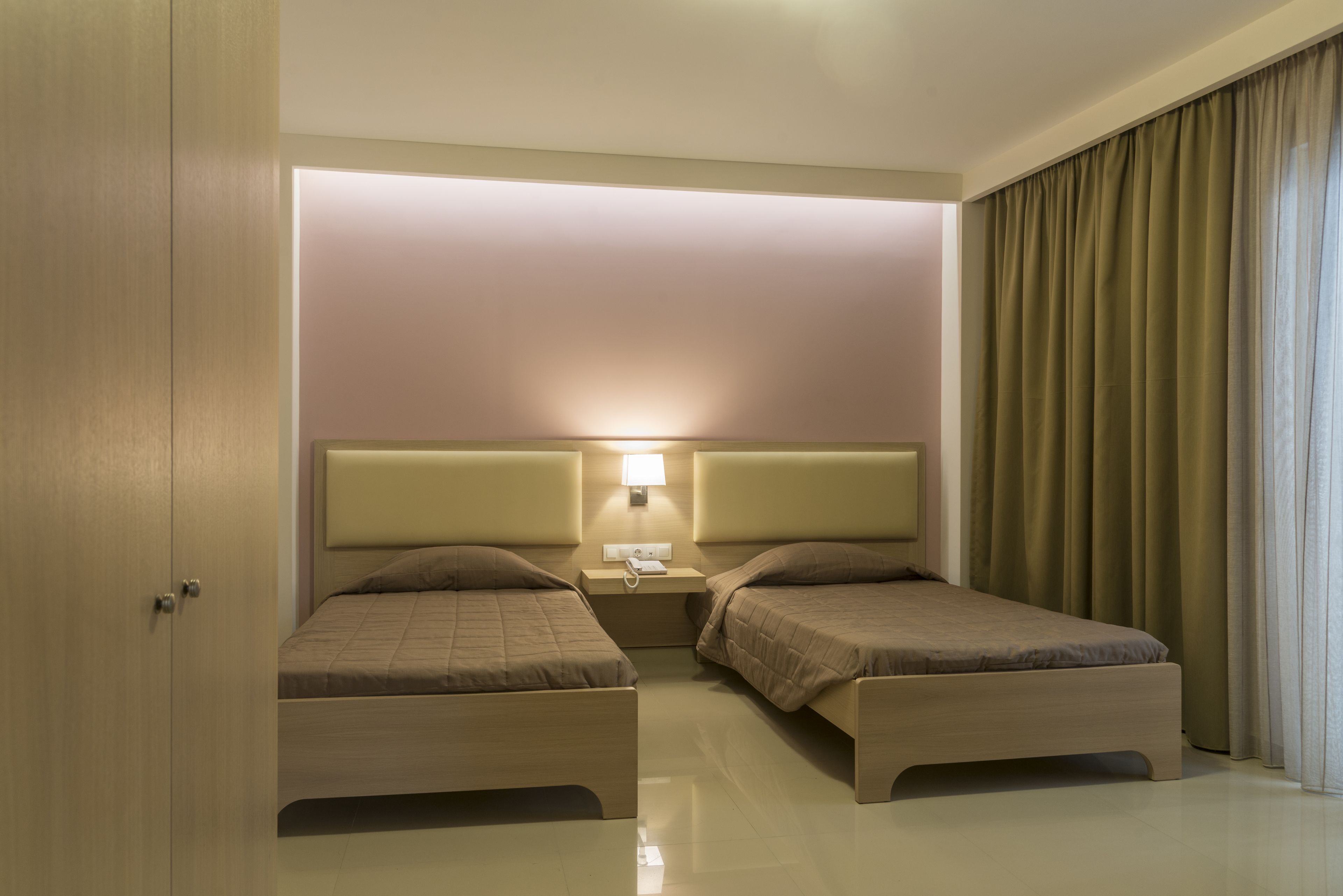 A hotel room with two beds, a nightstand with a lamp, and a large window with curtains.