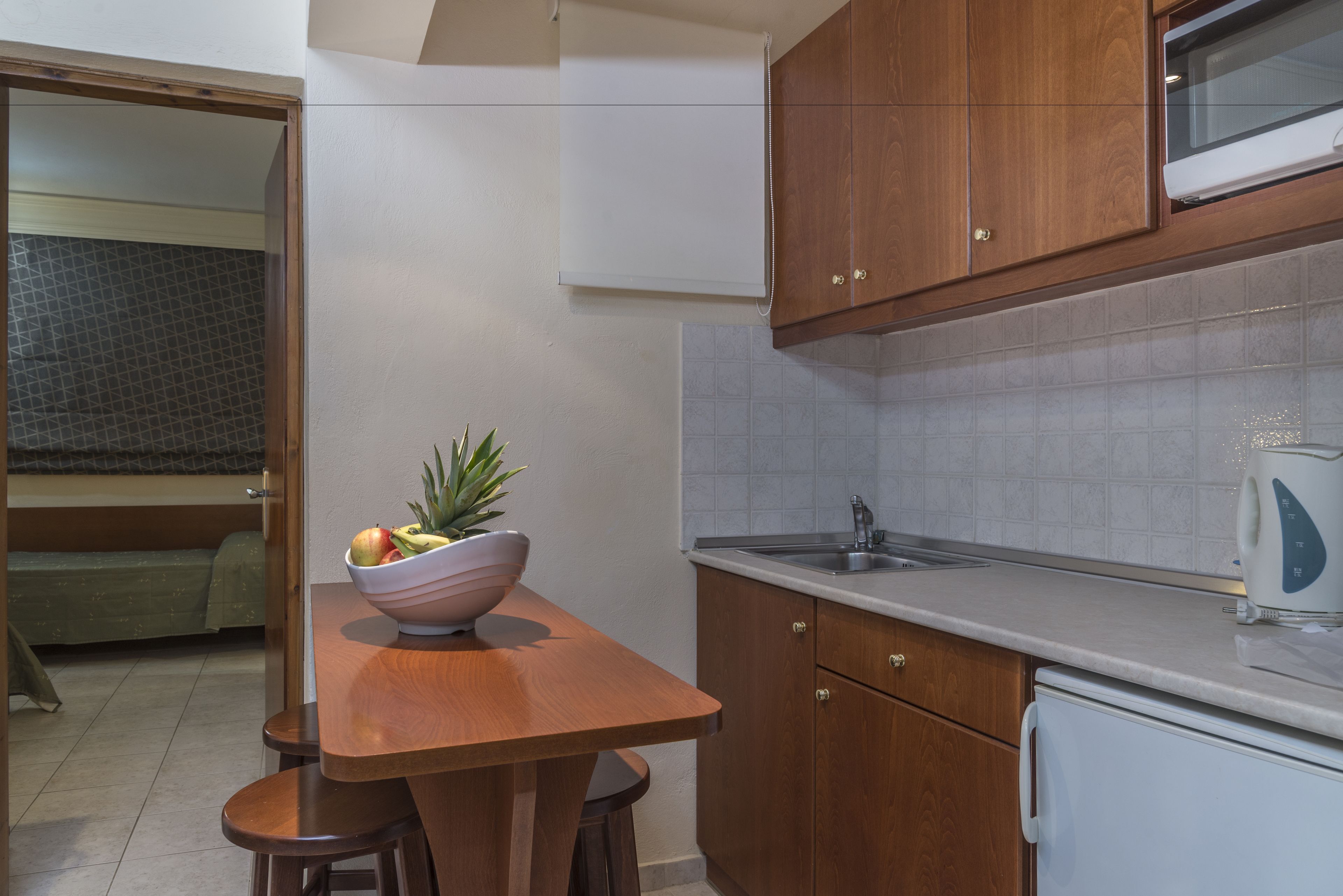 A compact kitchen with wooden cabinets, a white countertop, a sink, and a microwave.