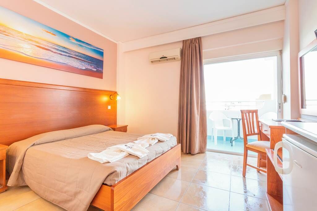 Habitación de hotel con cama, escritorio, silla, un cuadro y vistas a través de una ventana.