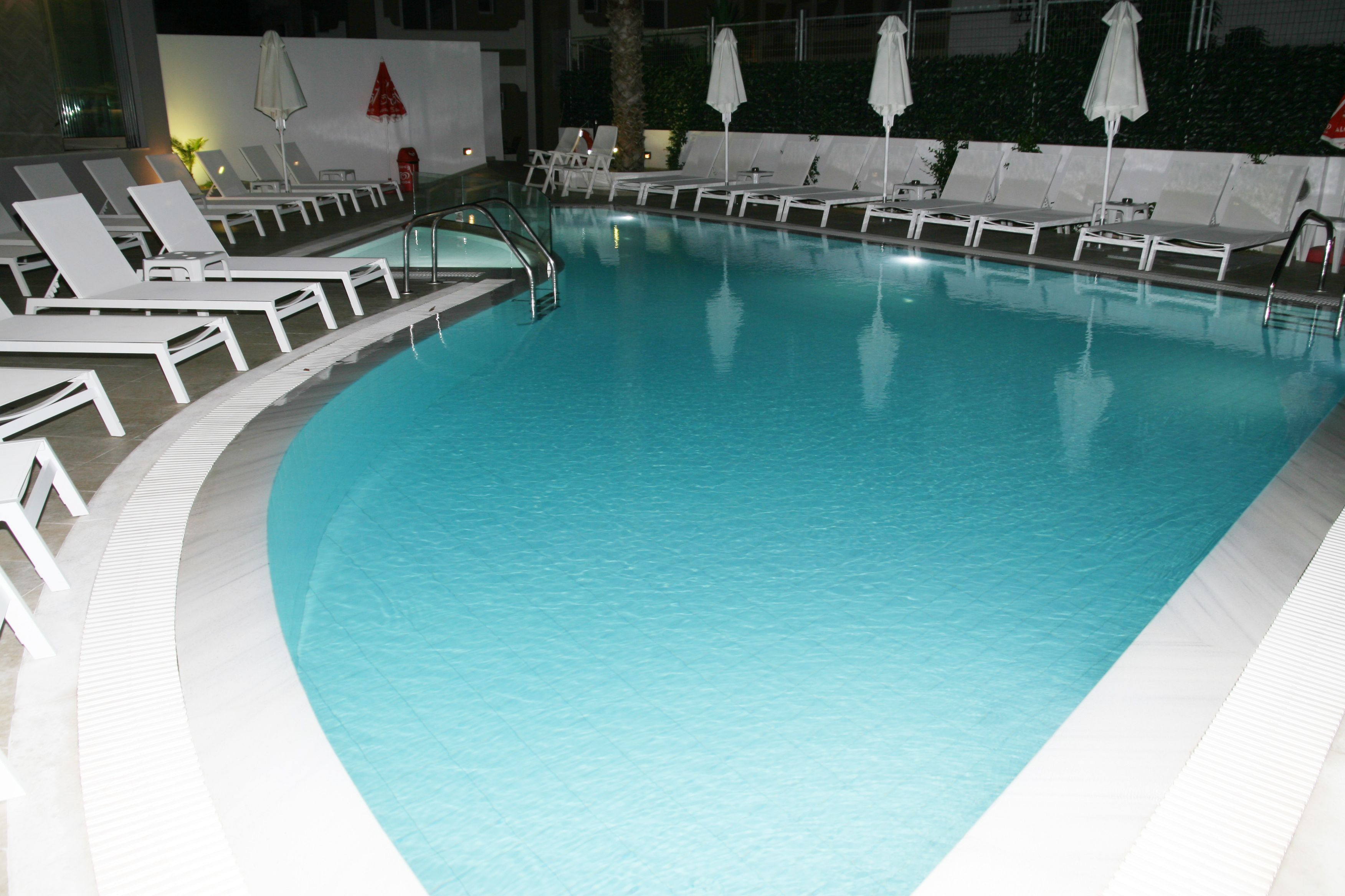 Una piscina con sillones blancos y sombrillas.