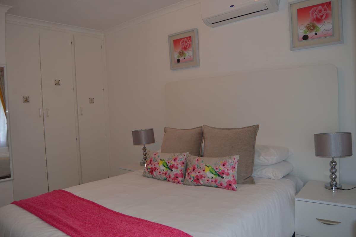 A hotel room with a bed, two bedside tables, a wardrobe, and two wall-mounted air conditioning units.